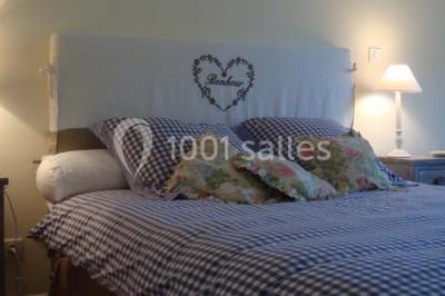 Salle à manger avec table dressée, chaises transparentes, poutre apparente, canapé bleu et tableaux au mur.