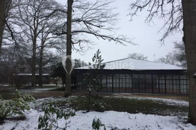 Salle à manger avec table dressée, chaises transparentes, poutre apparente, canapé bleu et tableaux au mur.