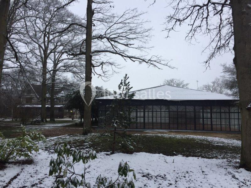 Serre vitrée entourée d'arbres dans un parc enneigé en hiver.