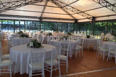 Salle à manger avec table dressée, chaises transparentes, poutre apparente, canapé bleu et tableaux au mur.