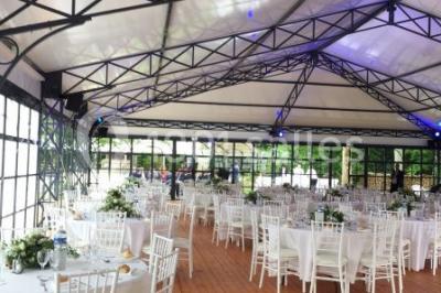 Salle à manger avec table dressée, chaises transparentes, poutre apparente, canapé bleu et tableaux au mur.