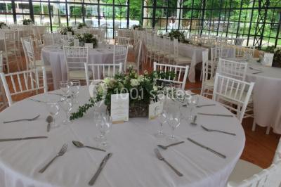Salle à manger avec table dressée, chaises transparentes, poutre apparente, canapé bleu et tableaux au mur.