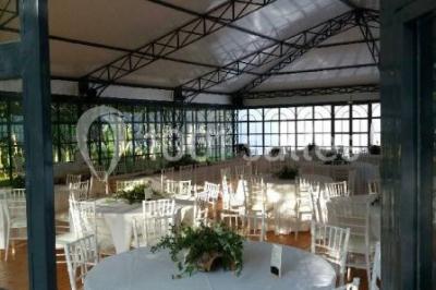 Salle à manger avec table dressée, chaises transparentes, poutre apparente, canapé bleu et tableaux au mur.