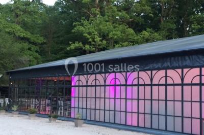 Salle à manger avec table dressée, chaises transparentes, poutre apparente, canapé bleu et tableaux au mur.