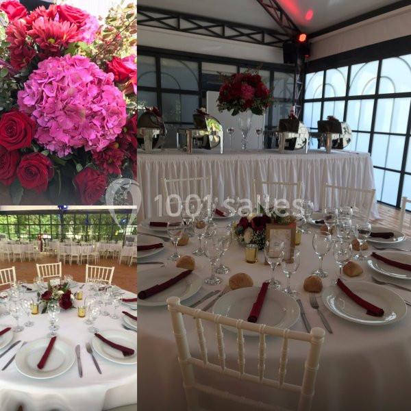 Salle de réception décorée avec des tables dressées, nappes blanches, serviettes rouges et compositions florales.