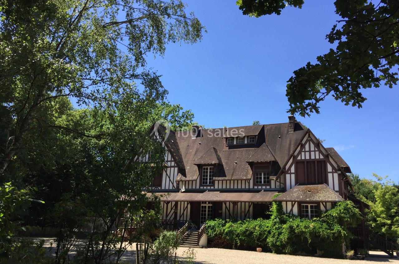 Maison à colombages entourée de végétation, avec un ciel bleu dégagé en arrière-plan.