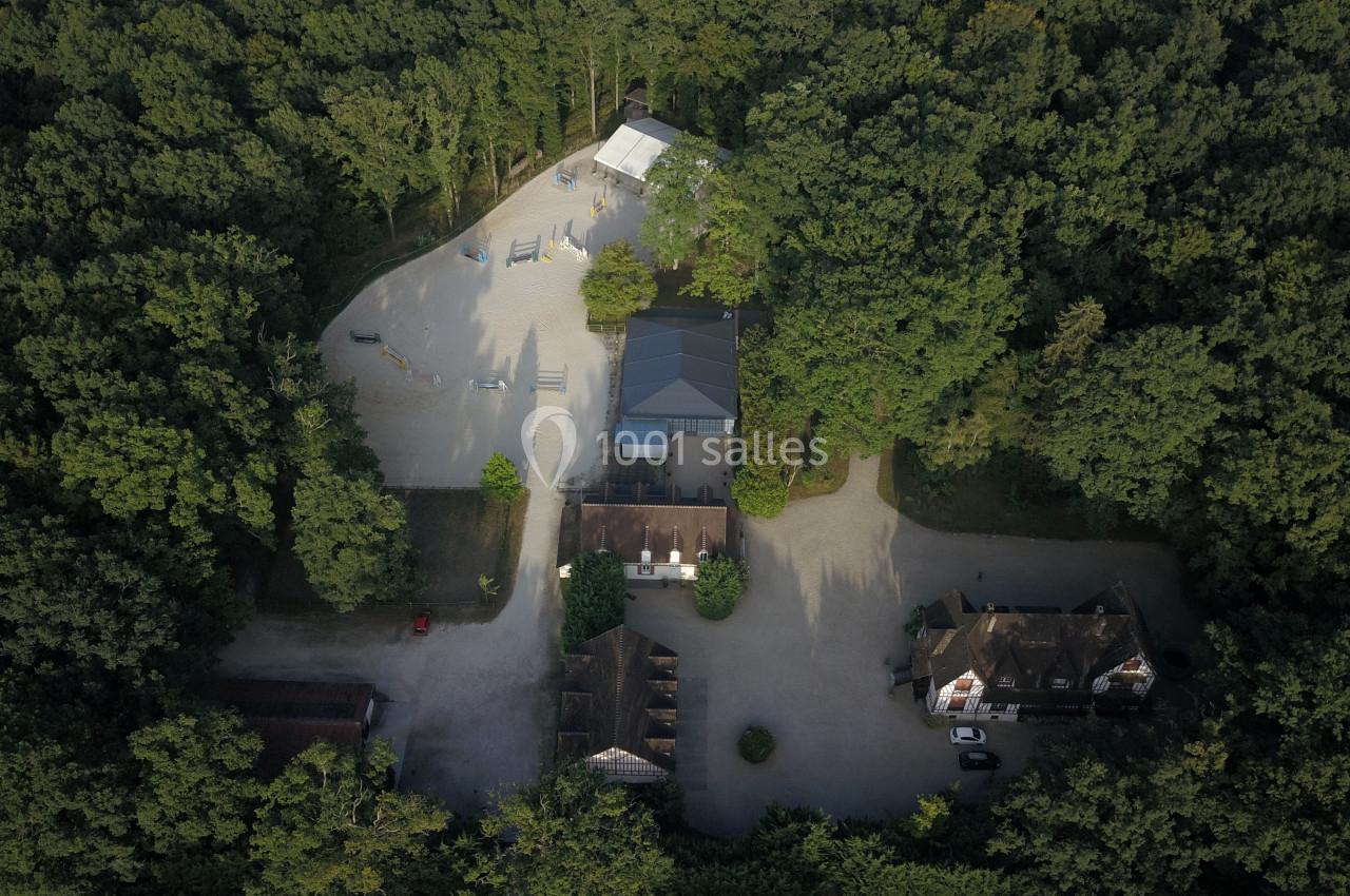 Vue aérienne d'un complexe entouré de forêt, comprenant des bâtiments, une carrière équestre et des chemins.