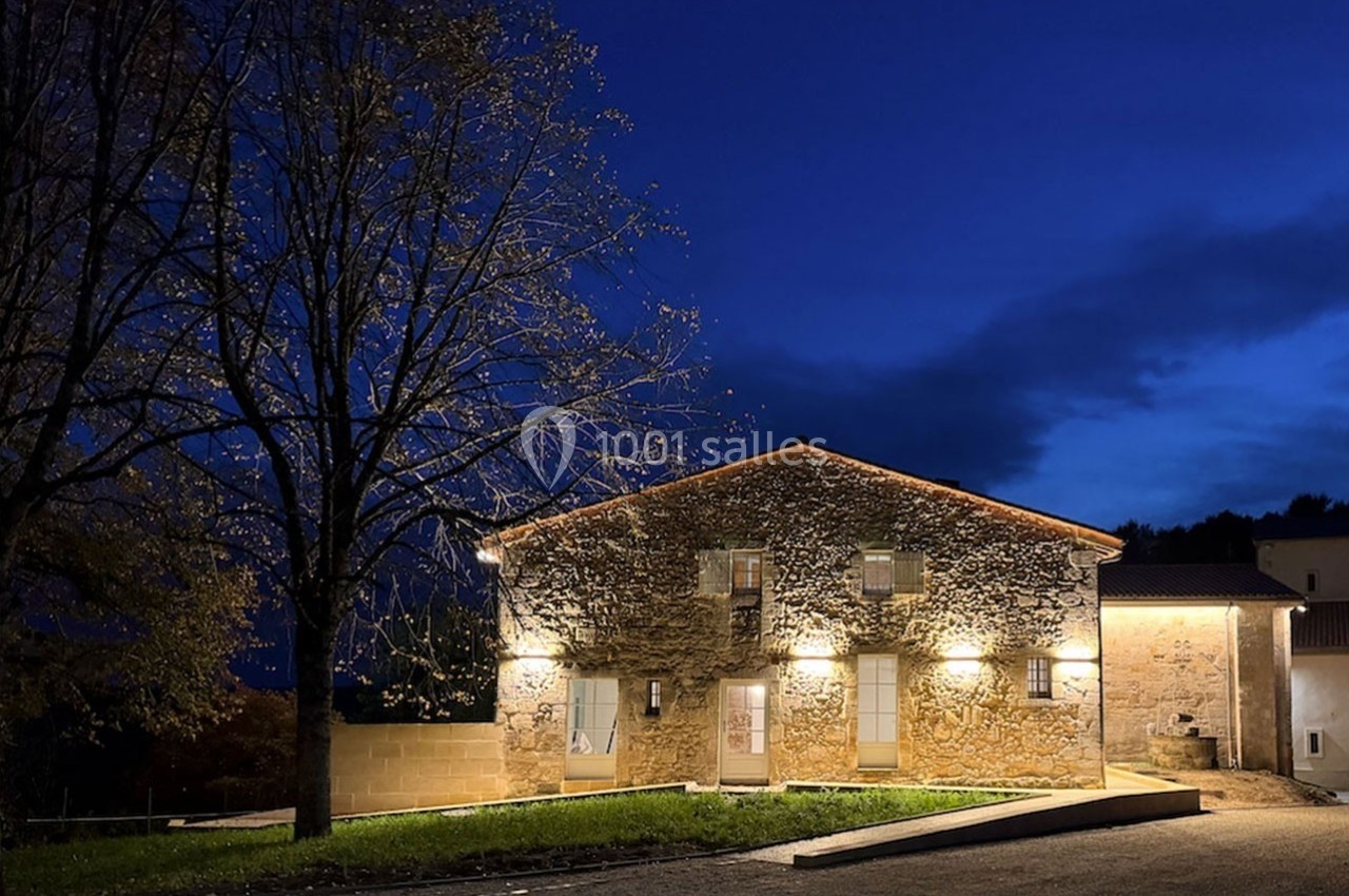 Bâtiment en pierre éclairé la nuit, entouré d'arbres et situé sous un ciel bleu foncé.