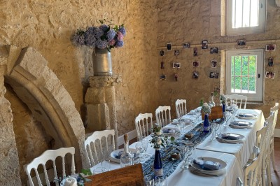 Salle de réception rustique avec murs en pierre, poutres apparentes, décorations florales et lumière naturelle.