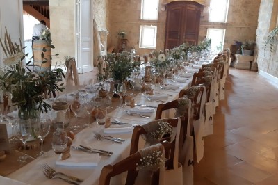 Salle de réception rustique avec murs en pierre, poutres apparentes, décorations florales et lumière naturelle.