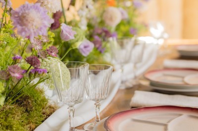 Bouteille de vin rosé posée sur une table décorée de fleurs, entourée de verres et d'assiettes.