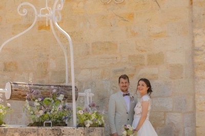 Bouteille de vin rosé posée sur une table décorée de fleurs, entourée de verres et d'assiettes.