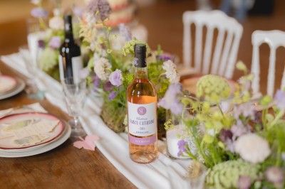 Bouteille de vin rosé posée sur une table décorée de fleurs, entourée de verres et d'assiettes.