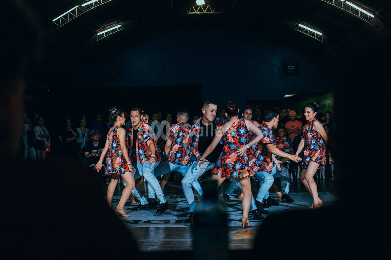 Un groupe de danseurs en tenues colorées exécute une chorégraphie sur une scène devant un public.