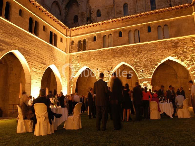 Personnes rassemblées de nuit dans une cour éclairée par des lumières chaudes, entourée d'arches en pierre.