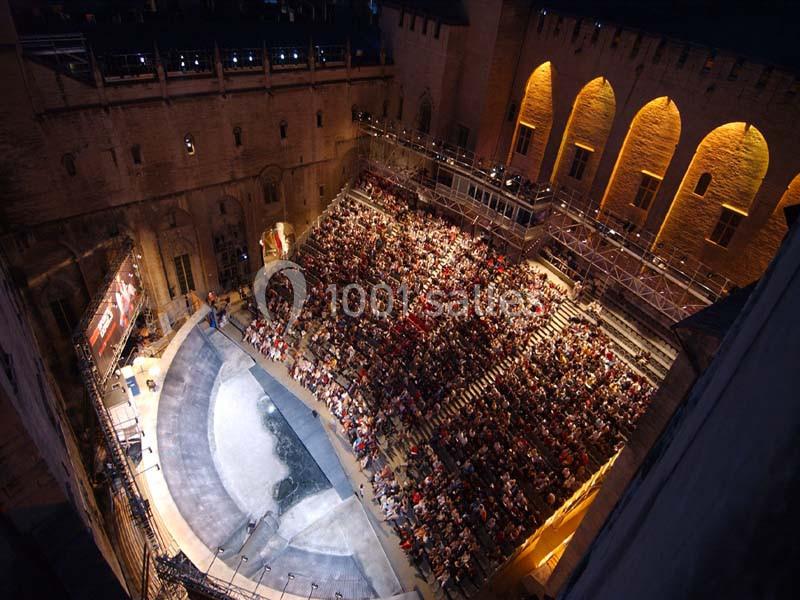 Vue aérienne d'un amphithéâtre en plein air rempli de spectateurs, entouré de murs historiques éclairés.