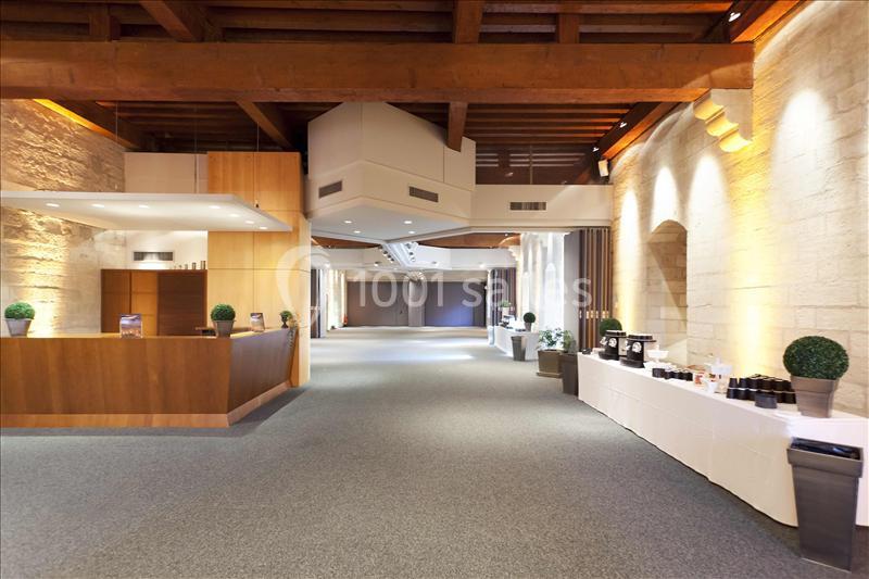 Salle spacieuse avec murs en pierre, plafond en bois, comptoir en bois et tables dressées pour un événement.