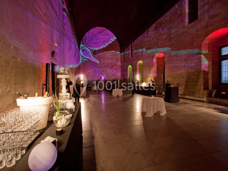 Salle voûtée en pierre éclairée par des projections colorées, avec tables dressées et buffet en premier plan.