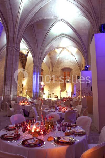 Salle voûtée éclairée en tons chauds, aménagée avec des tables rondes décorées pour un événement festif.