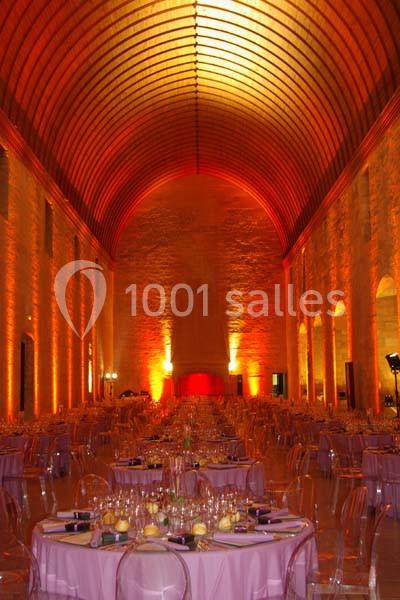 Grande salle voûtée illuminée en orange, aménagée avec des tables rondes dressées pour un événement.