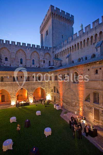 Cour intérieure d'un château médiéval éclairée en soirée, avec des tables dressées et des invités rassemblés.