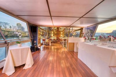 Salle de restaurant sur un bateau avec tables rondes dressées, nappes blanches et vue sur un paysage fluvial.