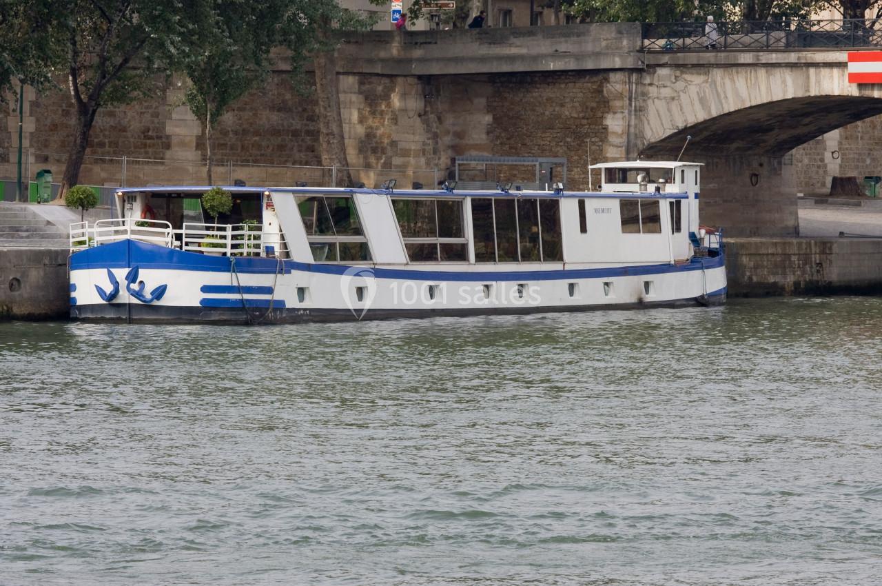 Bateau blanc et bleu amarré le long d'un quai en pierre, près d'un pont en arc.