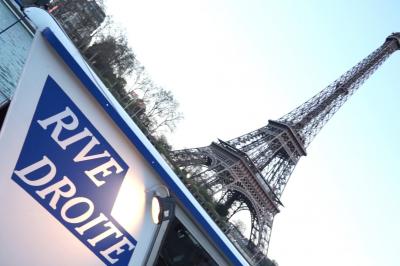 Salle de restaurant sur un bateau avec tables rondes dressées, nappes blanches et vue sur un paysage fluvial.
