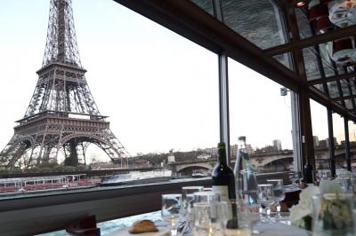 Salle de restaurant sur un bateau avec tables rondes dressées, nappes blanches et vue sur un paysage fluvial.