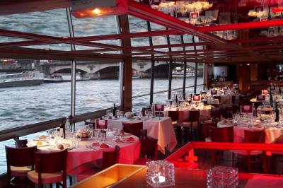 Salle de restaurant sur un bateau avec tables rondes dressées, nappes blanches et vue sur un paysage fluvial.