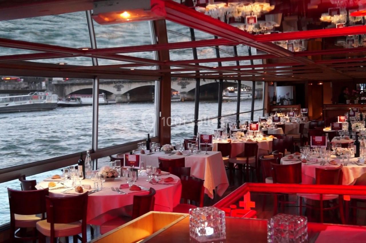 Salle de restaurant avec tables dressées, baies vitrées donnant sur une rivière et un pont visible à l'extérieur.