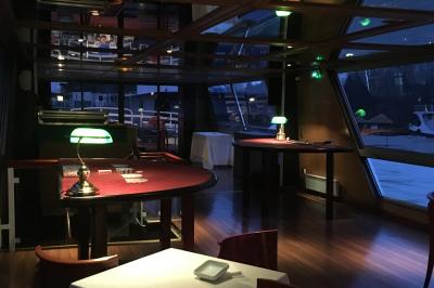 Salle de restaurant sur un bateau avec tables rondes dressées, nappes blanches et vue sur un paysage fluvial.