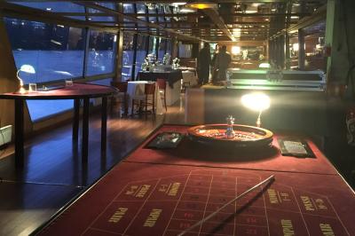 Salle de restaurant sur un bateau avec tables rondes dressées, nappes blanches et vue sur un paysage fluvial.
