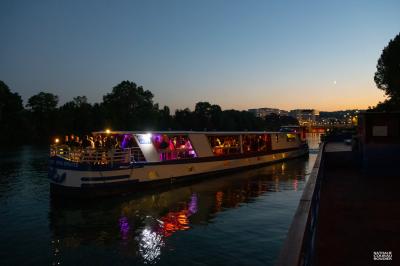 Salle de restaurant sur un bateau avec tables rondes dressées, nappes blanches et vue sur un paysage fluvial.
