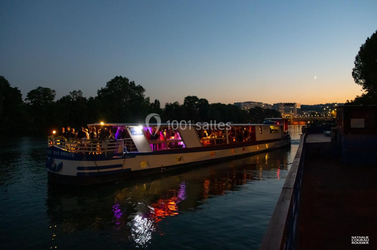 Bateau illuminé naviguant sur une rivière au crépuscule, avec des passagers profitant d'une ambiance festive.