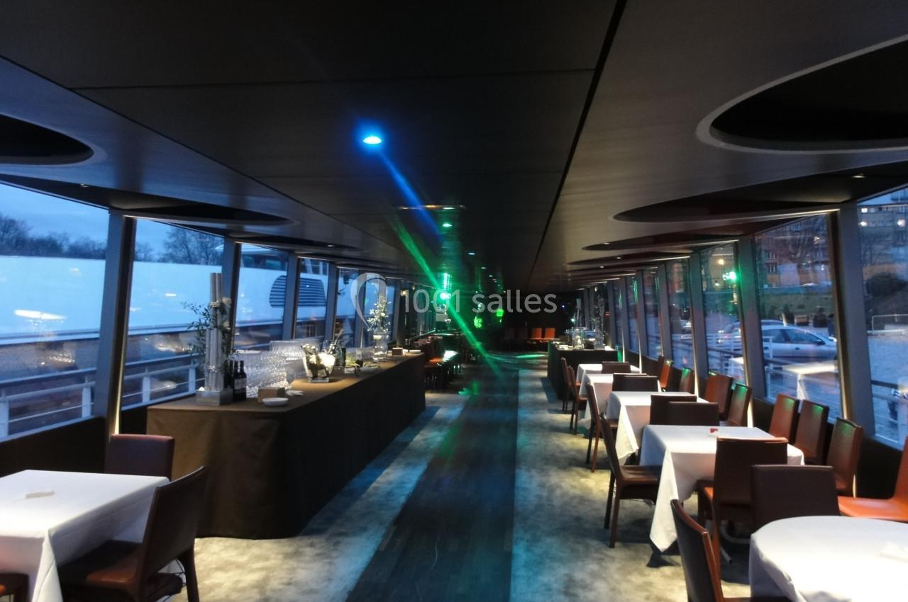 Salle de restaurant moderne avec tables dressées, grandes baies vitrées et buffet éclairé par des lumières colorées.