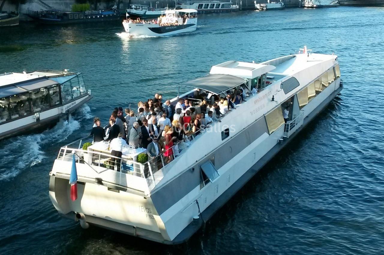 Bateau touristique rempli de passagers naviguant sur une rivière par temps ensoleillé.