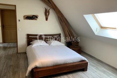 Lit double avec draps blancs dans une chambre mansardée, parquet au sol et poutres apparentes.