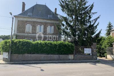 Lit double avec draps blancs dans une chambre mansardée, parquet au sol et poutres apparentes.