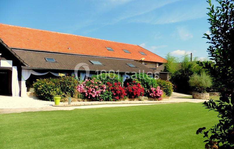 Bâtiment avec toit en tuiles rouges, entouré de buissons fleuris et d'une pelouse bien entretenue sous un ciel dégagé.