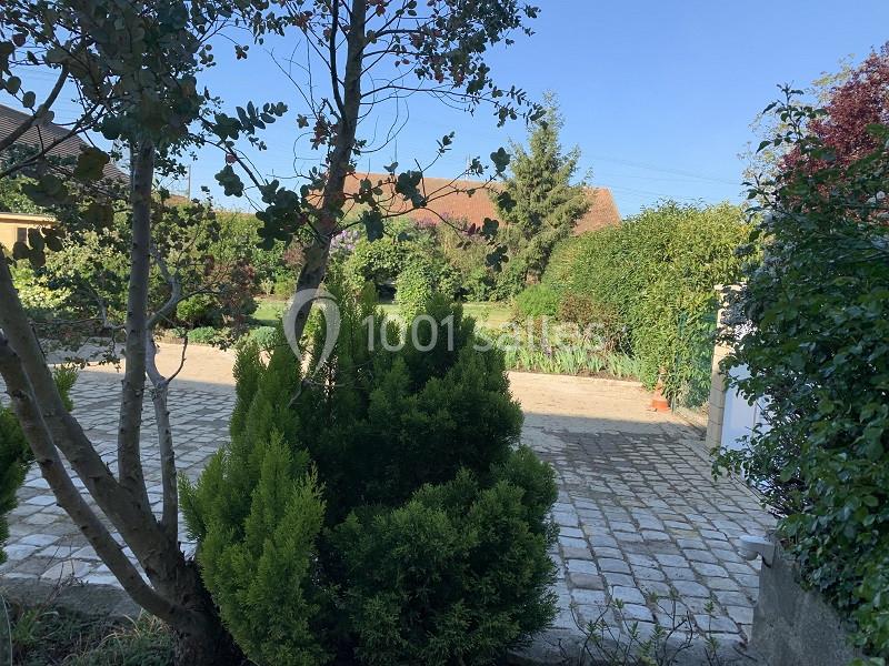 Allée pavée bordée de végétation avec des arbres, arbustes et une maison en arrière-plan sous un ciel dégagé.