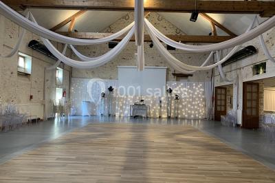 Lit double avec draps blancs dans une chambre mansardée, parquet au sol et poutres apparentes.