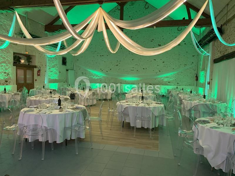 Salle de réception décorée avec des nappes blanches, des chaises transparentes et un éclairage vert tamisé.