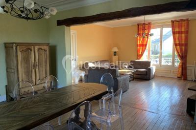 Lit double avec draps blancs dans une chambre mansardée, parquet au sol et poutres apparentes.