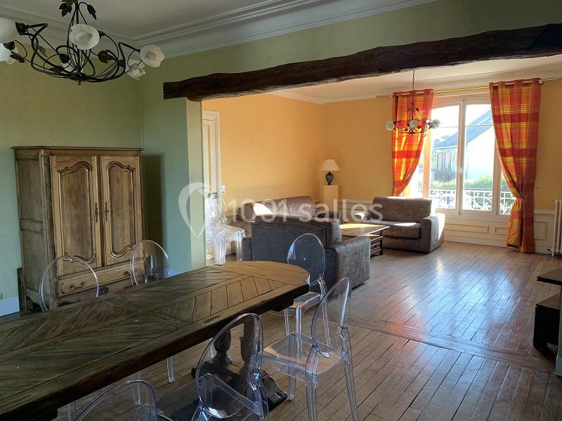 Salle de séjour lumineuse avec parquet, table en bois, chaises transparentes, canapés et grandes fenêtres avec rideaux…
