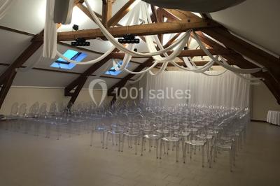 Lit double avec draps blancs dans une chambre mansardée, parquet au sol et poutres apparentes.