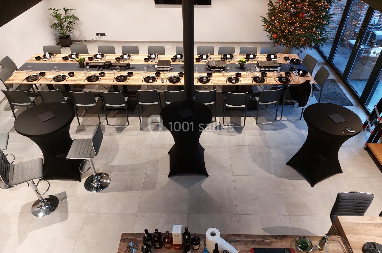 Salle moderne avec une grande table dressée pour un repas, des tables hautes et un sapin décoré en arrière-plan.