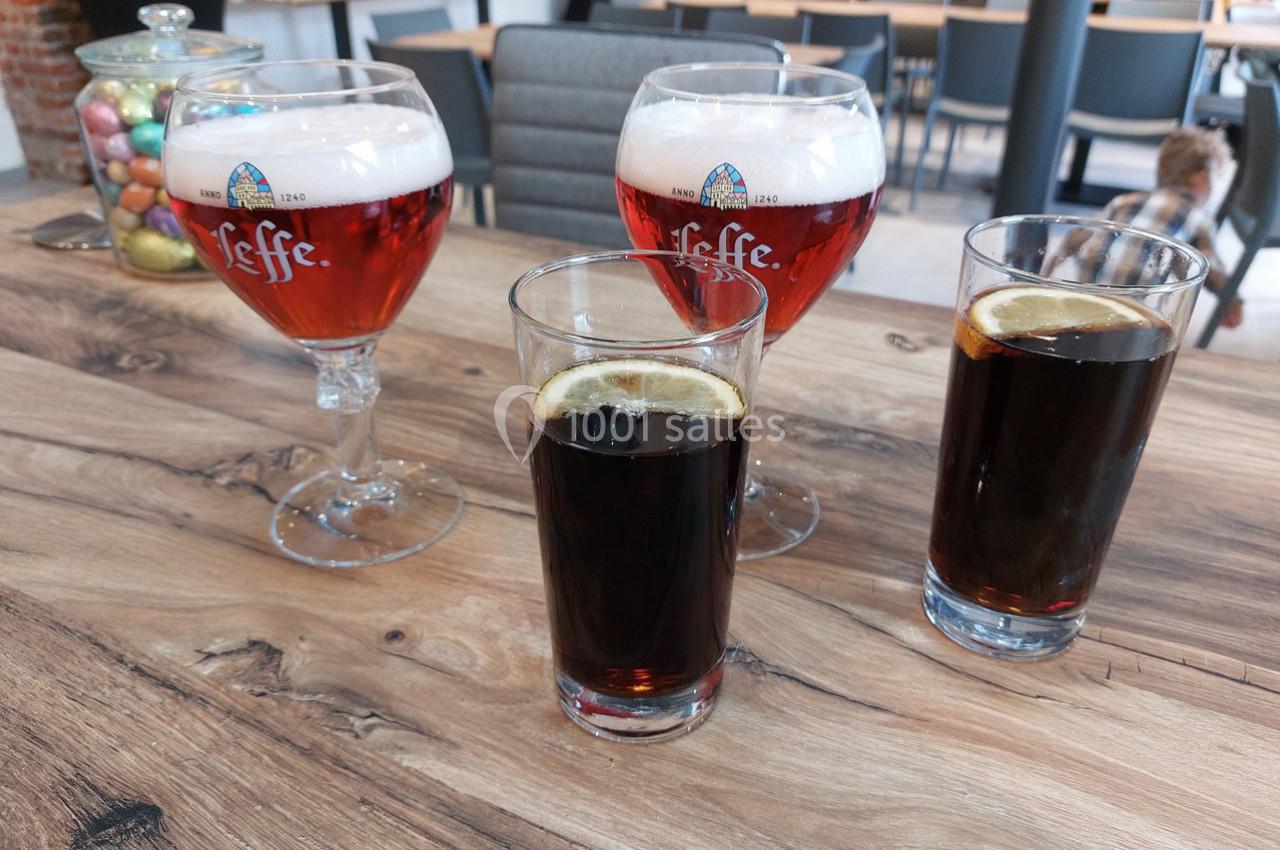 Quatre verres posés sur une table en bois : deux bières ambrées et deux sodas bruns avec rondelles de citron.