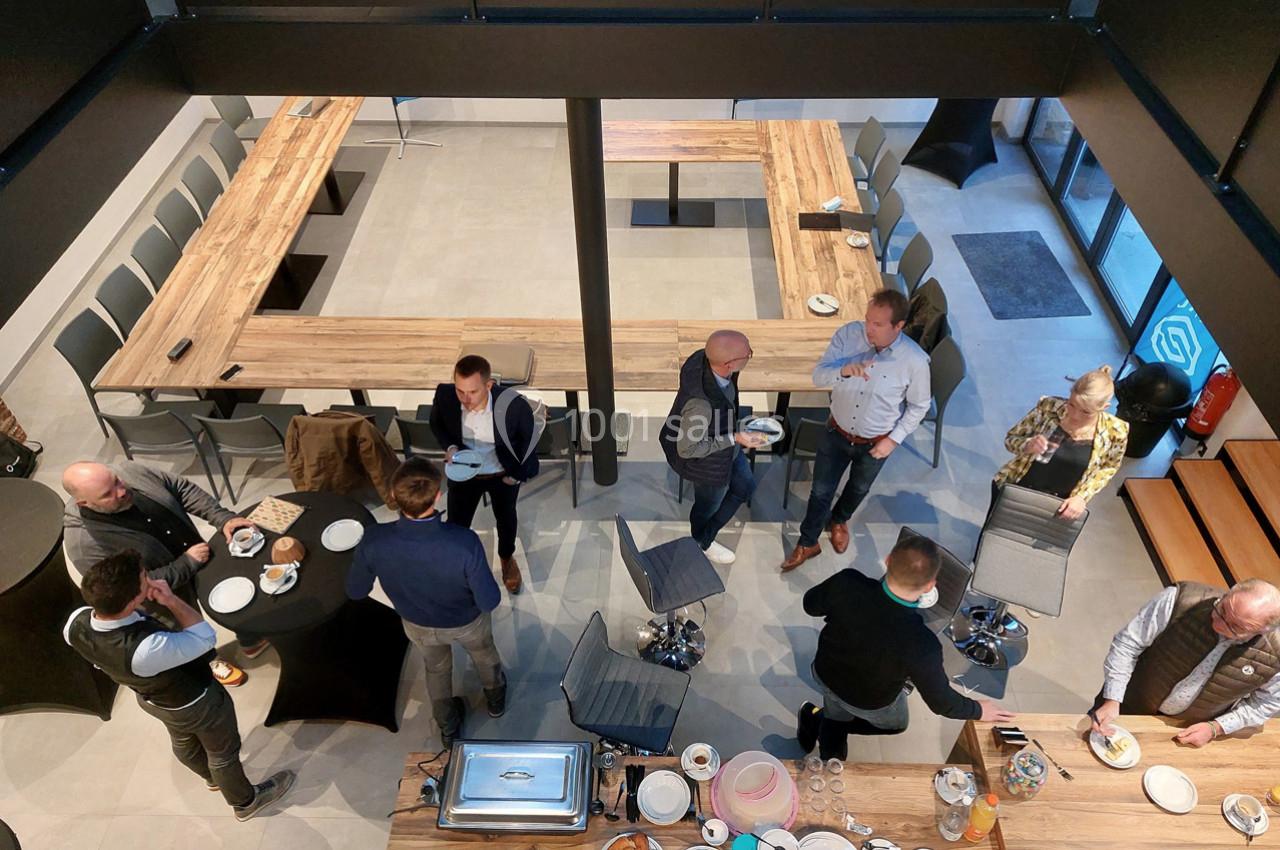 Personnes debout dans une salle de réunion, discutant et partageant un buffet autour de tables en bois disposées en U.