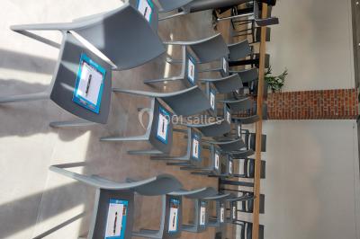 Salle de réunion moderne avec chaises disposées en rangées, tables hautes et grandes baies vitrées laissant entrer la…